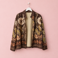 Chaqueta Dalia estampada floral en tonos marrones sobre percha blanca y fondo rosa pastel